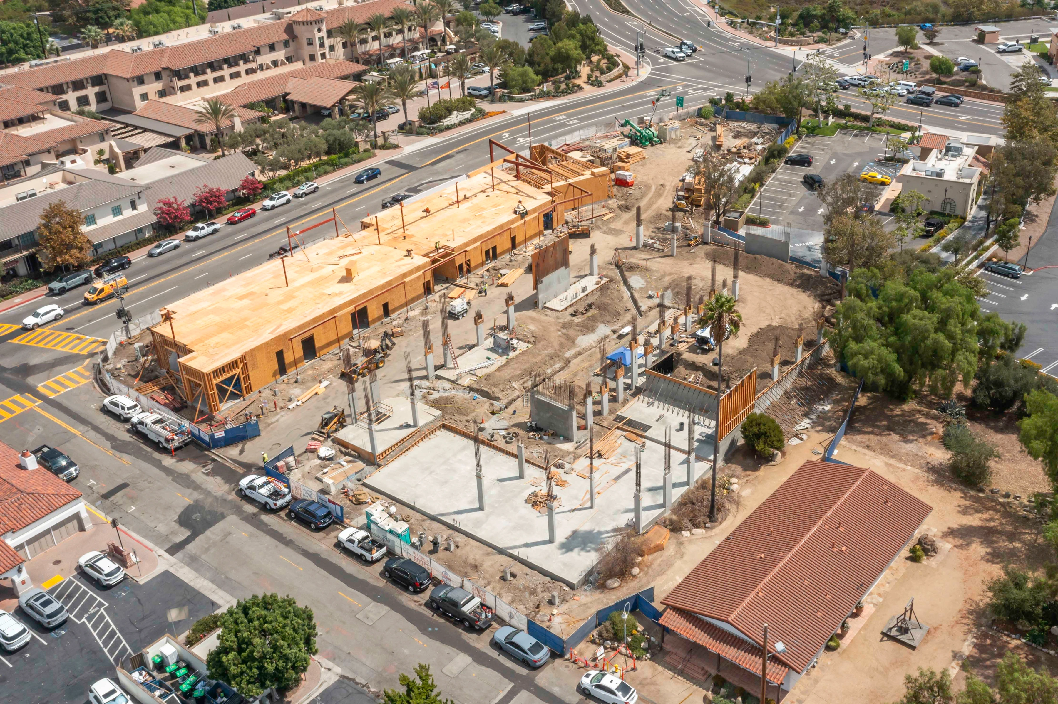 Mission Place construction site with a long wood-sheathed structure, open wall openings, concrete slabs, columns and graded soil.