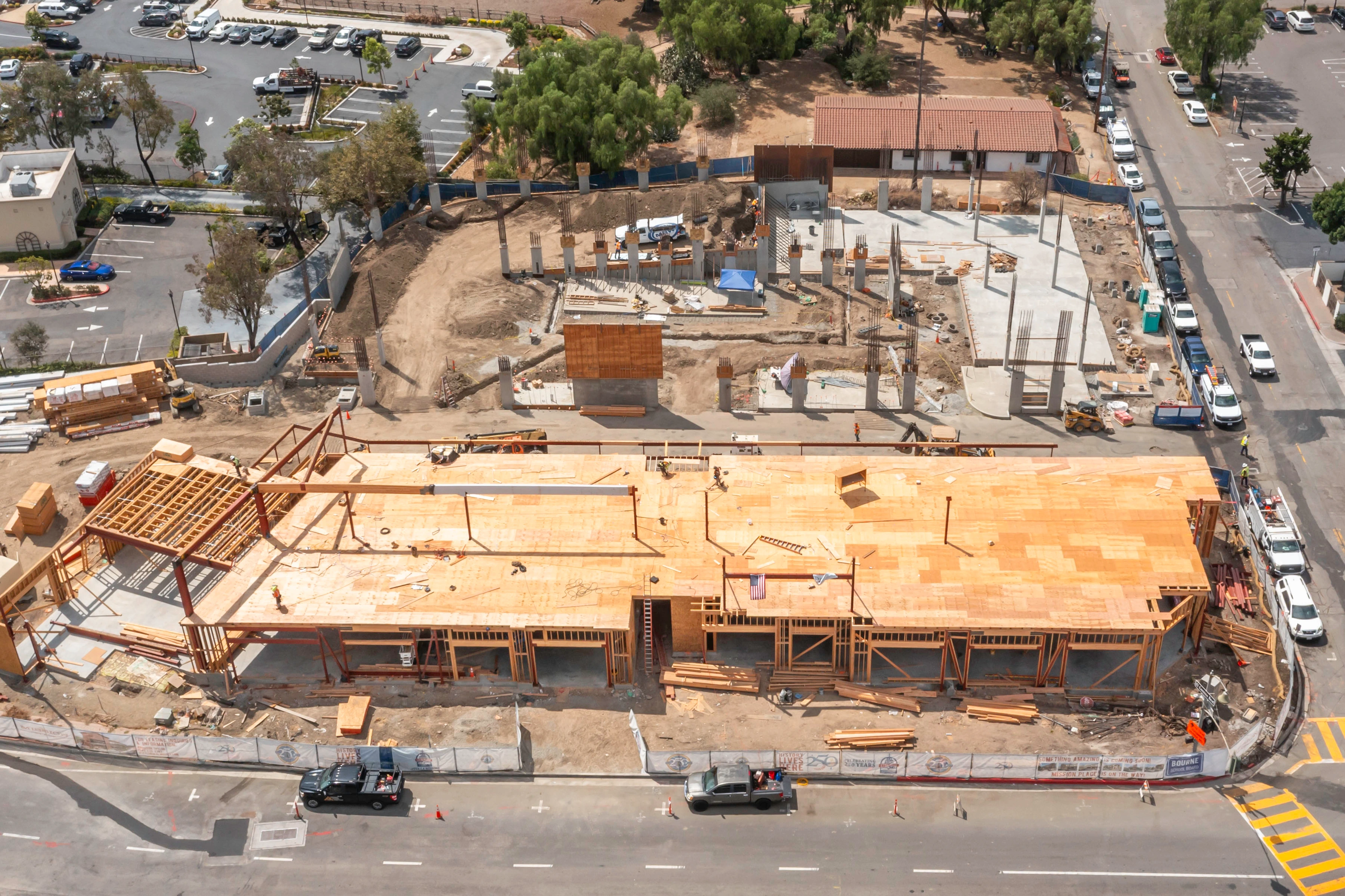 Broad plywood deck with exposed steel members above it and concrete columns with reinforcing steel farther across the Mission Place site.