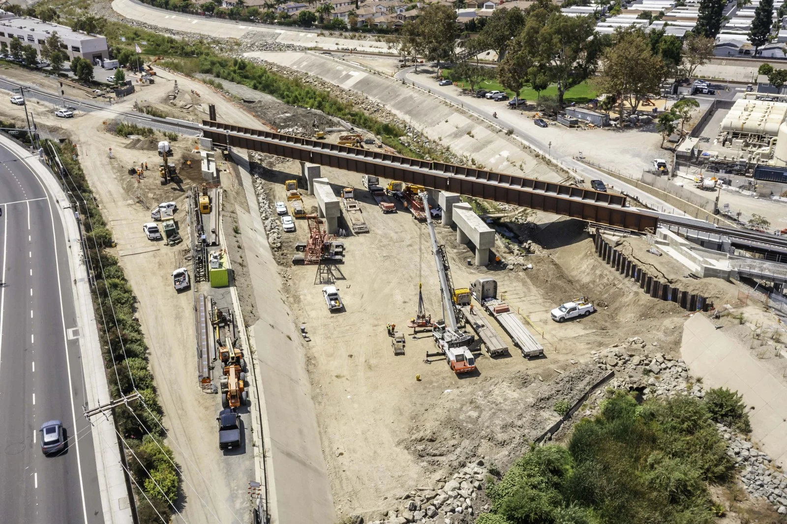 Elevated diagonal view of the rust-brown steel bridge span, concrete supports, equipment and excavated channel at the San Juan Creek project.